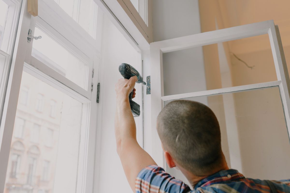 Hausmeister stellt mit dem Akkuschrauber einen Fensterbeschlag nach